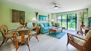 Amplia sala de estar con un sofá verde, sillas de madera, una mesa de comedor con sillas y un ventanal con vistas al exterior.
