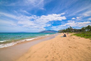Una playa con cielos despejados, mar tranquilo y algunas personas.