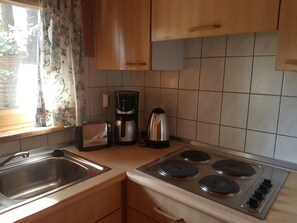A kitchen with a sink, stove, toaster, coffee maker, and kettle.