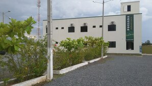 A building with a green signboard, a gravel driveway, and some greenery. - Pousada Chef Brasil (Barra Velha)
