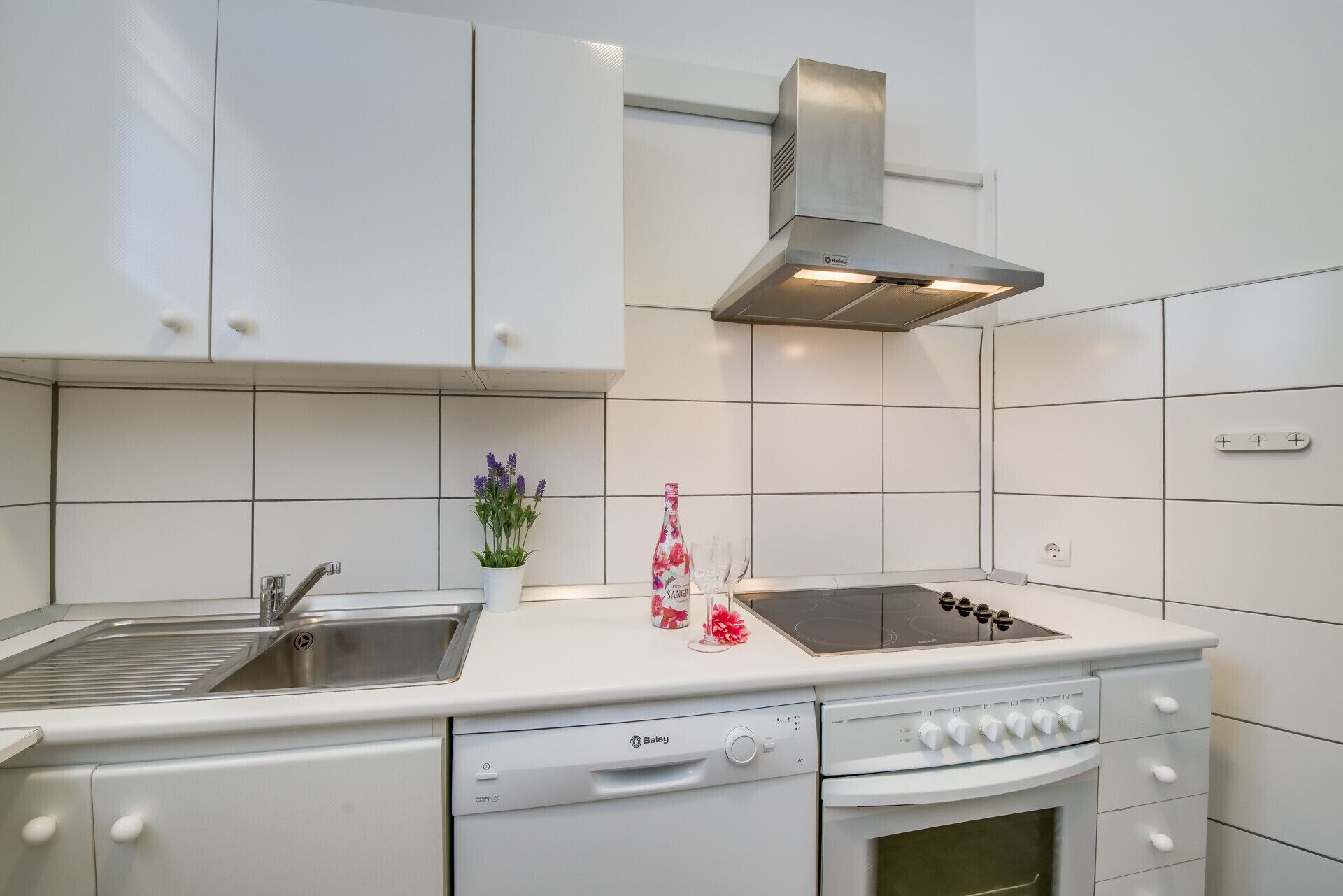 Une cuisine avec des meubles blancs, une hotte de cuisinière en acier inoxydable, un four encastré et un lave-vaisselle.