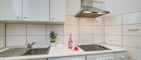 Une cuisine avec des meubles blancs, une hotte de cuisinière en acier inoxydable, un four encastré et un lave-vaisselle.