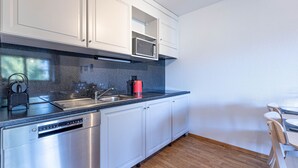A modern kitchen with white cabinets, a stainless steel dishwasher, a microwave, and a red kettle. - Pracondu 2 304 - OUTDOOR & FUN  apartment 6 pers (Haute-Nendaz)