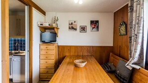 Uma cozinha compacta com uma mesa de madeira, televisão e um pequeno frigorífico.