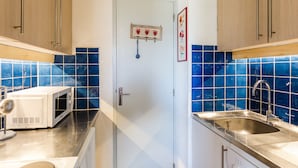 Cozinha com azulejos azuis, micro-ondas, pia e armários de madeira.