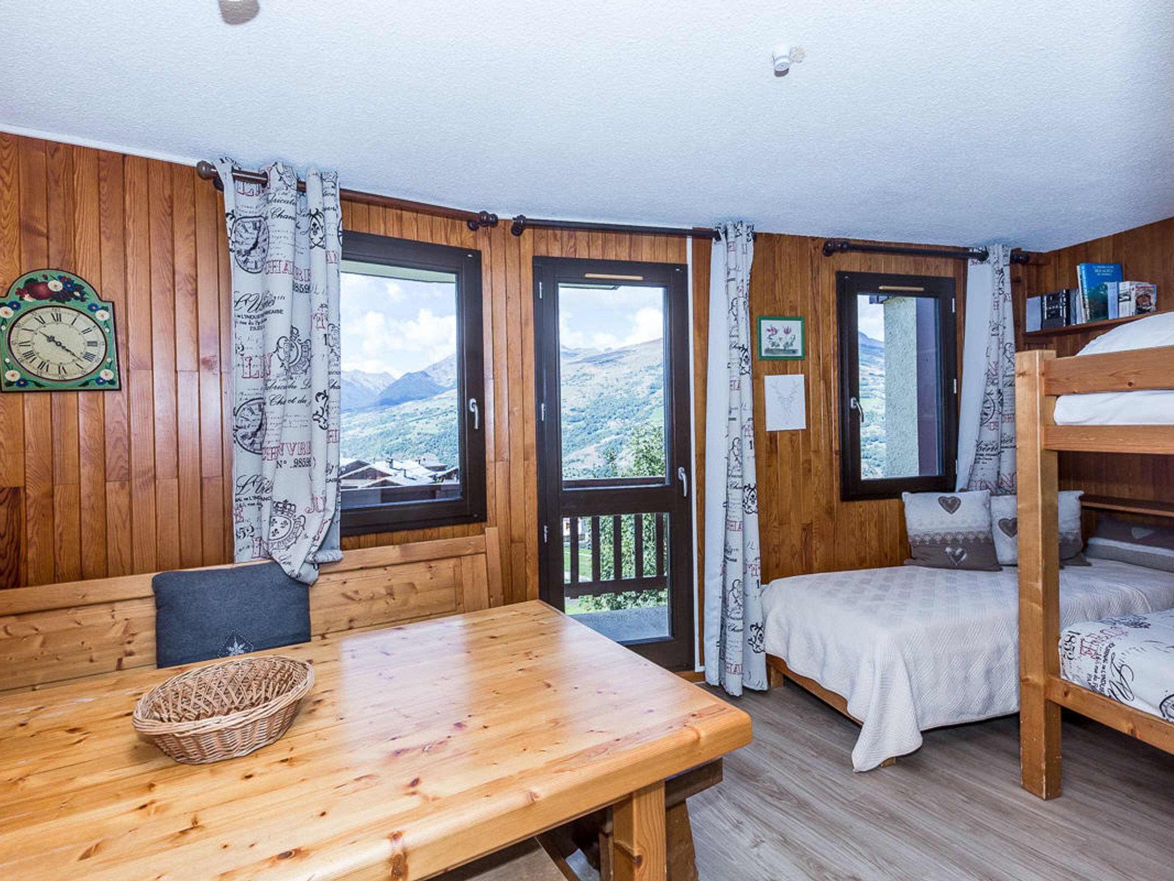 A wooden cabin with a dining table, bunk beds, and large windows offering mountain views.
