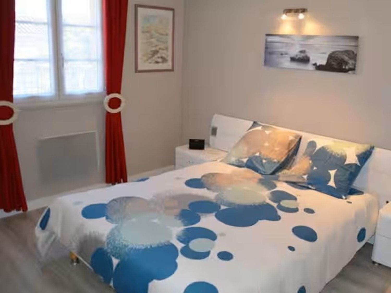 Een slaapkamer met een bed, nachtkastjes, een raam met gordijnen en wanddecoratie.