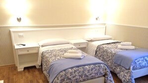 A hotel room with two single beds, each with floral-patterned bedding and white pillows. There is a nightstand with a remote control and a drawer. The room has wooden flooring and a white headboard. - Delightful studio apartment right in the center (Firenze)