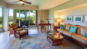 A spacious living room with a large sliding glass door leading to a balcony, a ceiling fan, a dining area with a table and chairs, and a sofa with decorative pillows. - Beautiful Vista Waikoloa B105 - Renovated in 2018! (Waikoloa)