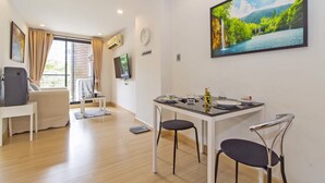 Een moderne kamer met een eettafel, twee stoelen, een bank, een televisie en een groot raam met gordijnen.