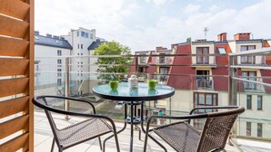 Un balcón con una mesa de vidrio, dos sillas de mimbre y vistas a edificios cercanos.