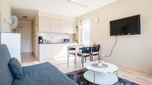 Una sala de estar moderna con un sofá, una mesa de comedor con sillas, una zona de cocina y un televisor montado.