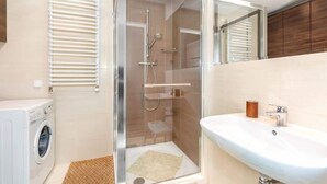 Un baño moderno con ducha envuelta en vidrio, lavadora integrada y un lavamanos.