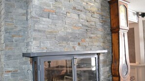 Una chimenea de piedra con puerta de cristal, repisa de madera y un reloj de pie.