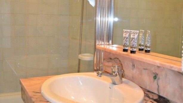 Un baño con lavamanos de mármol, cabina de ducha de vidrio y artículos de tocador sobre la encimera.