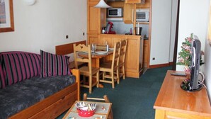 Un espacio habitable compacto con sofá, una pequeña mesa de comedor, zona de cocina con armarios de madera, microondas y televisión.