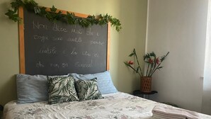 Una cama bien hecha con ropa de cama floral, una pizarra con texto en italiano y una pequeña mesa con una planta.