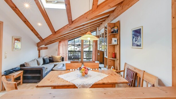 Une pièce chaleureuse avec un plafond en bois, une table à manger sur laquelle se trouve un panier de fruits, un canapé et une bibliothèque.