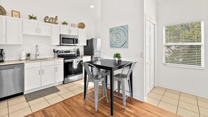 Une cuisine moderne avec des meubles blancs, des appareils en acier inoxydable et un coin repas comprenant une table noire et des chaises grises.