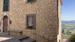 Un edificio de piedra con puerta de madera, contraventanas verdes y una ventana con celosías.