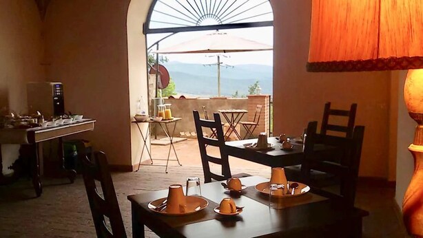 Comedor con mesas dispuestas para cuatro, zona de cocina con refrigerador y vistas al exterior a través de un arco.
