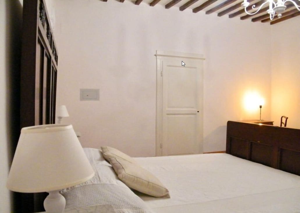 A bedroom with a bed, a nightstand, a lamp, a door, and a wall-mounted light fixture.