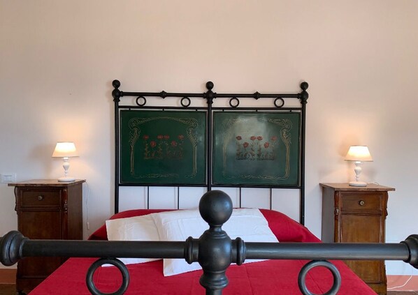 A bed with a black metal headboard, red bedding, and two bedside tables with lamps. - Casa Cerboneschi (Casale Marittimo)