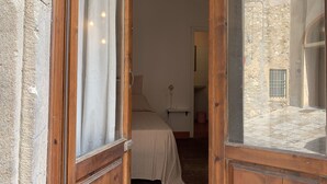 Una puerta de madera abierta que da a una habitación con una cama, una mesita y una pared de piedra.