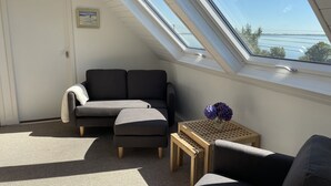 A room with a sloped ceiling, a black sofa, a small wooden table with a vase of flowers, and a view of the outdoors. -  Lakeside Lough Mask shore (Tourmakeady)