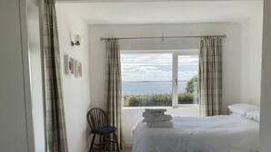 A bedroom with a bed, a chair, a radiator, a window with curtains, and a view of the sea. -  Lakeside Lough Mask shore (Tourmakeady)