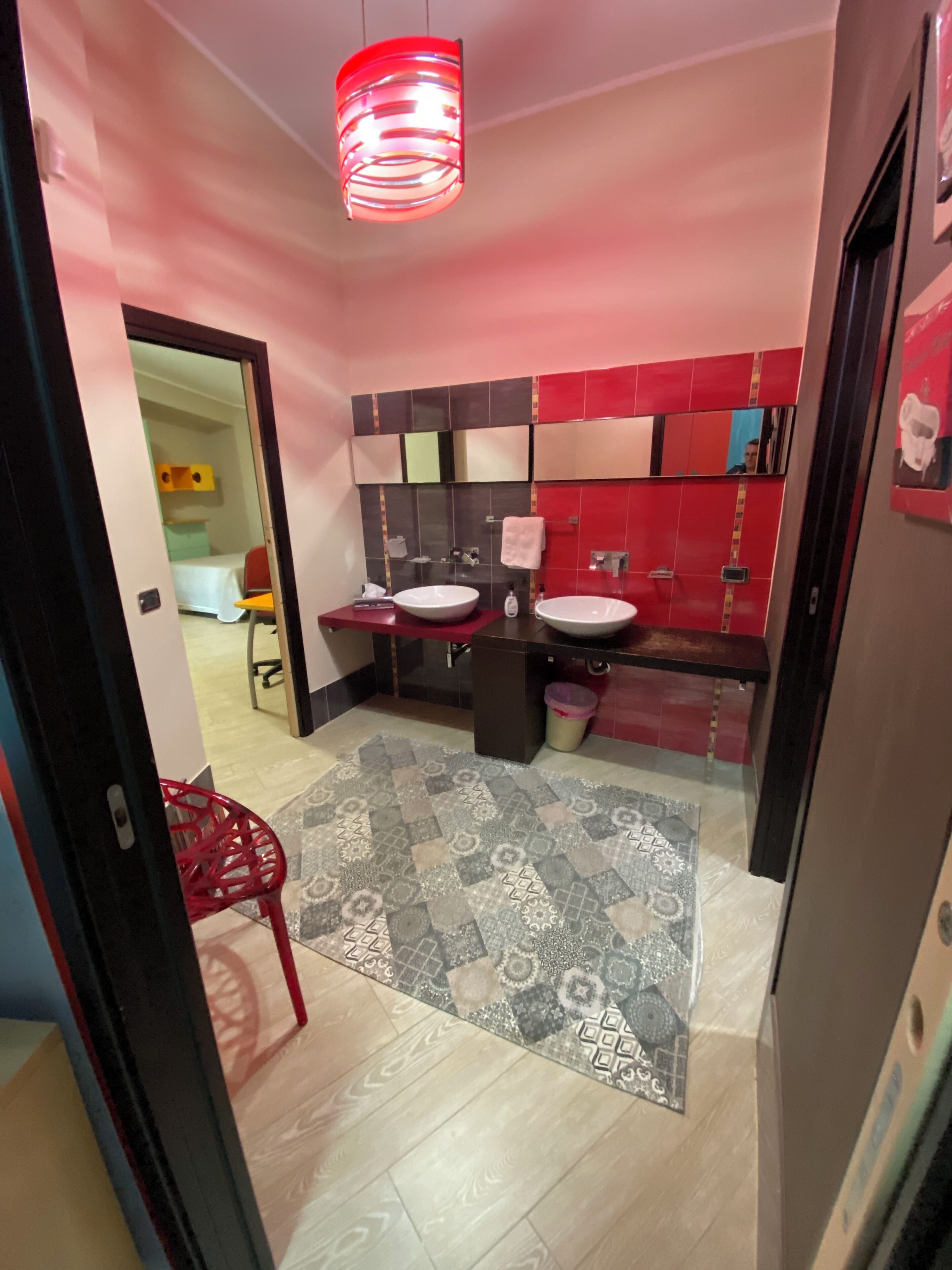 Un baño moderno con dos lavabos, un salpicadero de azulejos rojo y negro, y una alfombra estampada en el suelo.