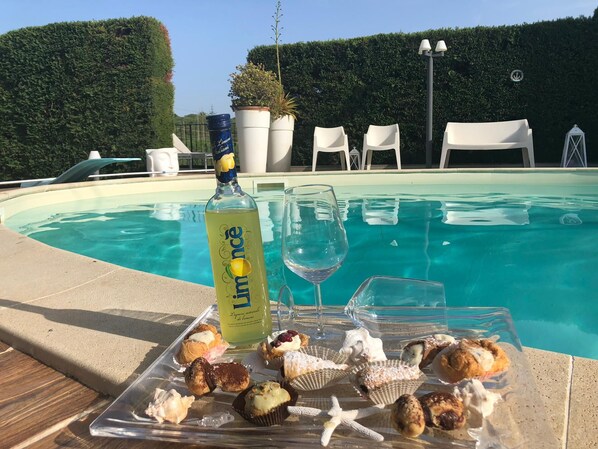 Ein Poolbereich mit einer Flasche Limonade, einem Weinglas und einer Platte mit Gebäck und Muscheln.