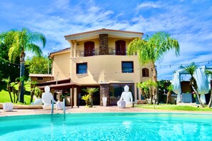 Ein zweistöckiges Haus mit Swimmingpool, umgeben von Palmen und blauem Himmel.