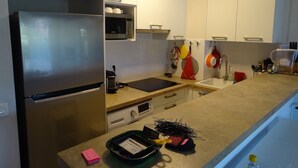 A modern kitchen with a stainless steel refrigerator, microwave, and a built-in oven. There is a sink with a faucet, a countertop with various kitchen items, and cabinets above the counter. - Comfortable apartment near the beach and services (Saint-Raphaël)