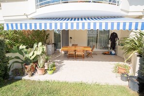 A patio with a table and chairs, surrounded by potted plants and a striped awning.