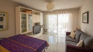 A room with a bed, a sofa, a TV on a stand, and a large window with curtains. - Comfortable apartment near the beach and services (Saint-Raphaël)