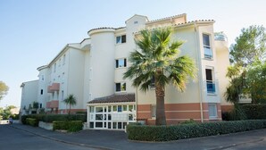 A multi-story hotel with a central entrance, palm trees, and a clear sky. - Comfortable apartment near the beach and services (Saint-Raphaël)