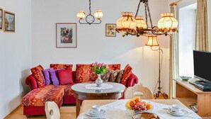 Ett mysigt vardagsrum med en röd, mönstrad soffa, ett runt soffbord med en vas med blommor och en tv-apparat som står på ett träställ.