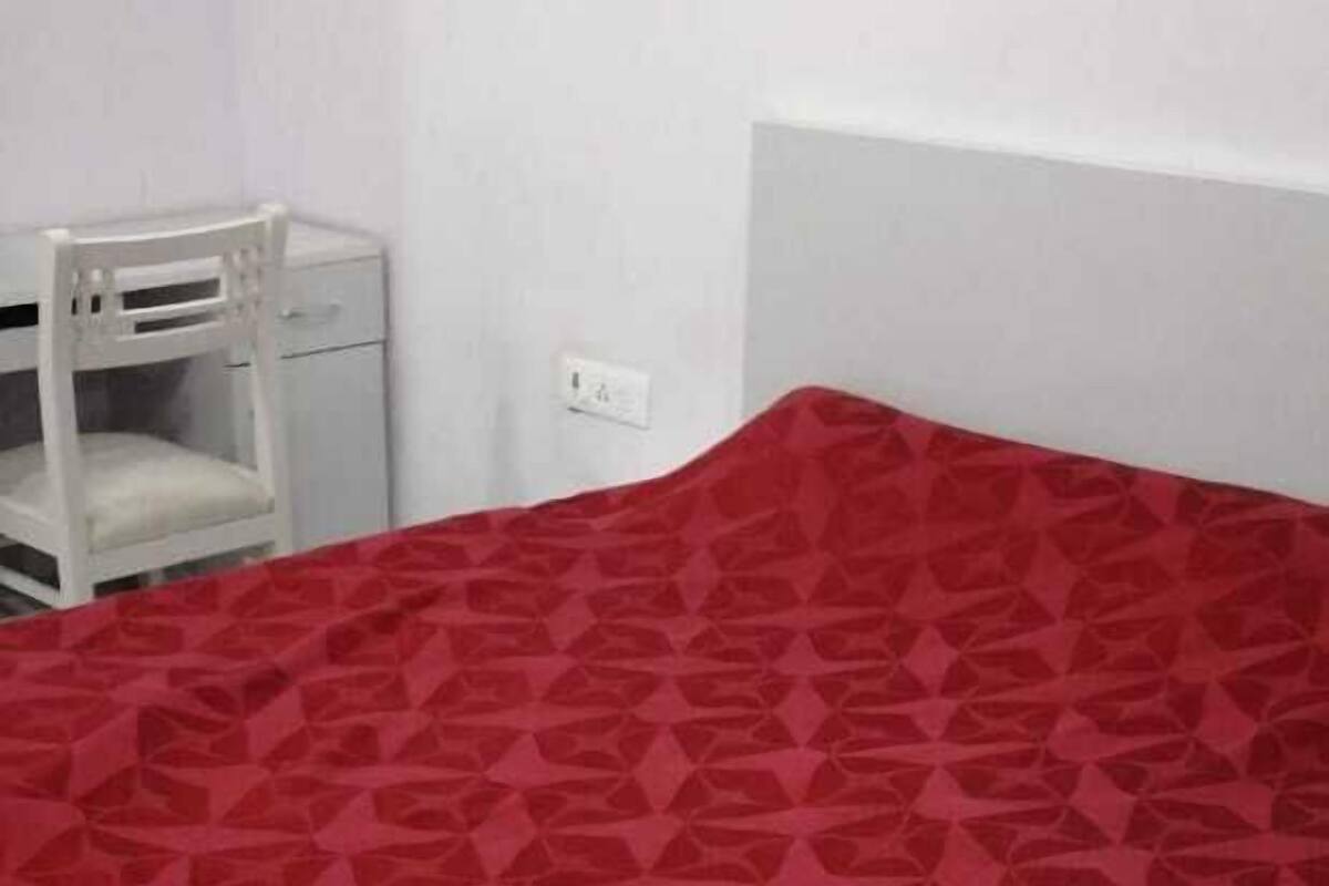 A bed with a geometric patterned bedspread in a room with white walls and a white nightstand.