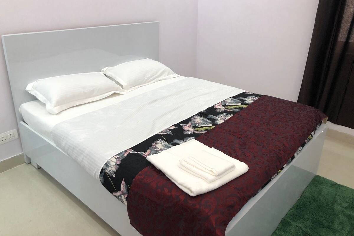 A bed with white bedding and a floral-patterned blanket, a white pillow, and a folded white towel on the bed.