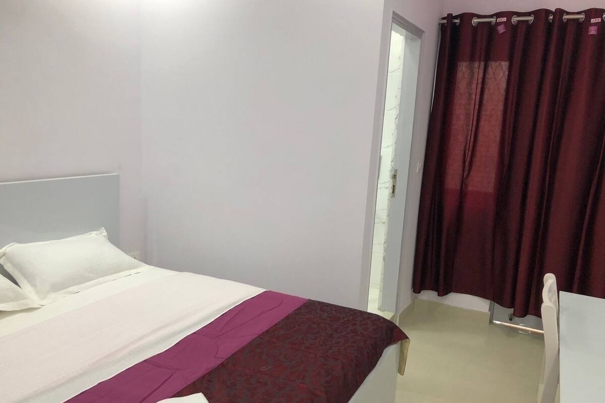 A bedroom with a bed, a chair, a door, and a curtain.