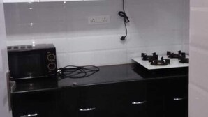 A compact kitchen with white cabinets, a black countertop, a toaster, and a gas stove. - Atul's Europa Apartments (New Delhi)