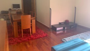 A room with a wooden dining table, chairs, a television, a small cabinet, and a red shaggy rug. - Apartment Braga Parque (Braga)