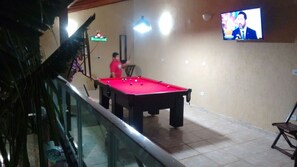 Uma mesa de bilhar em uma sala com uma televisão fixada na parede.