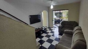A living room with a black and white checkered floor, a flat-screen TV mounted on the wall, and a sofa. - GATED COMMUNITY, 24-HOUR SECURITY, SWIMMING POOL WITH HYDROMASSAGE.  (Peruíbe - SP)