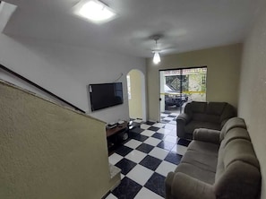 Uma sala de estar com chão xadrez em preto e branco, uma televisão de tela plana na parede e um sofá.