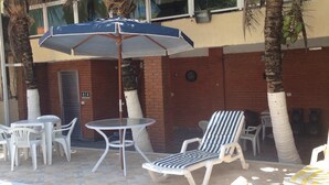 An outdoor seating area with a table and chairs, a striped lounge chair, and a blue umbrella. - GATED COMMUNITY, 24-HOUR SECURITY, SWIMMING POOL WITH HYDROMASSAGE.  (Peruíbe - SP)
