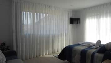 A hotel room with a bed, a TV mounted on the wall, and sheer curtains.