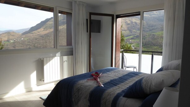 A bedroom with a bed, a TV, and a view of a mountainous landscape through large windows. - Studio with Jacuzzi "Balcony of the Len" (Soba)