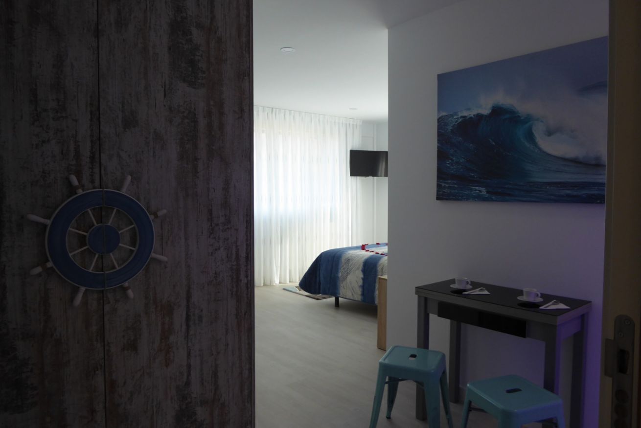 Una habitación con cama, escritorio, silla, televisor y un cuadro de una ola.